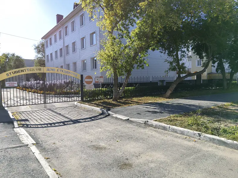 Въездные ворота с аркой «Студенттер үйі» и проходная, за ними корпус общежития