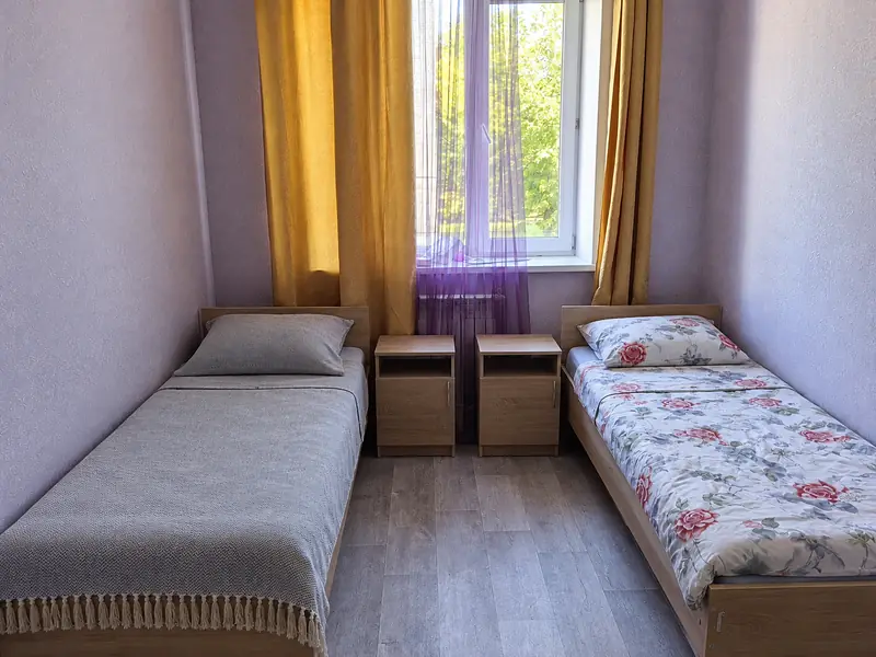 Комната на двоих: две кровати, тумбочки, окно со шторами